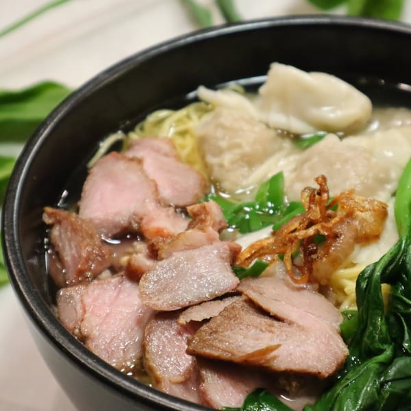 Close-up of a Vietnamese noodle soup with sliced pork, wontons, green onions, and fried shallots.