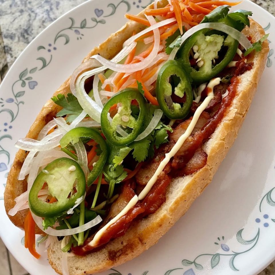 A Vietnamese Banh Mi sandwich, filled with meat, pickled vegetables, cilantro, and jalapeños, on a white plate.
