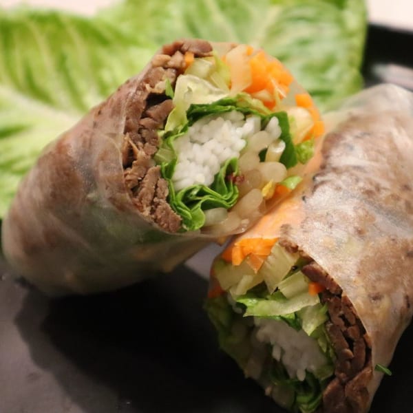 Two Vietnamese spring rolls, filled with meat, rice, lettuce, and carrots, on a dark surface.