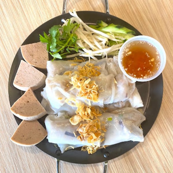 Vietnamese Banh Cuon with sliced pork, bean sprouts, herbs, and dipping sauce on a black plate.