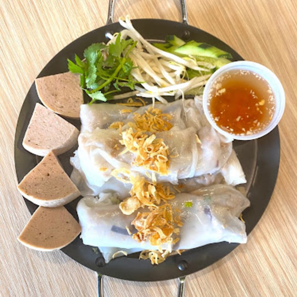 Vietnamese Banh Cuon with sliced pork, bean sprouts, herbs, and dipping sauce on a black plate.